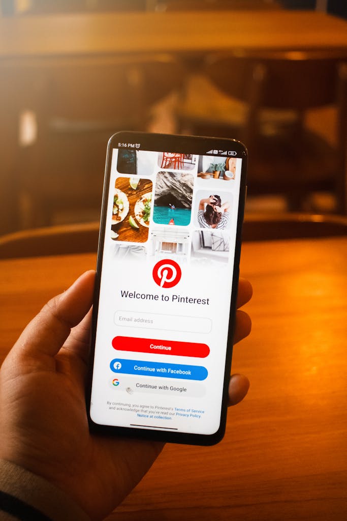 Close-up of a hand holding a smartphone displaying the Pinterest login screen indoors.